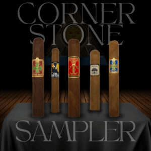 Cornerstone Sampler display with five Foundation cigars standing upright on a dark table. Bands include The Wise Man, The Upsetters, Highclere Castle Victorian, and Charter Oak. A stylized sun emblem and the words Cornerstone Sampler appear in the background.
