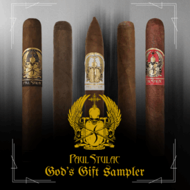 Five Paul Stulac cigars standing upright in a row on a dark gradient background. Each cigar has a distinct band design in gold, black, white, and red. Below the cigars is a golden Paul Stulac crest with wings and a skull, and the text “Paul Stulac God’s Gift Sampler” in a gothic font.