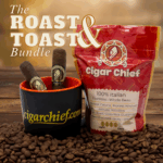 A promotional image for Cigar Chief’s Roast & Toast Bundle featuring two Maduro cigars resting in a black and orange mug with the Cigar Chief logo, alongside a red bag of 100% Italian Espresso Whole Bean Coffee. Coffee beans are scattered across the wooden surface with a warm, golden background.
